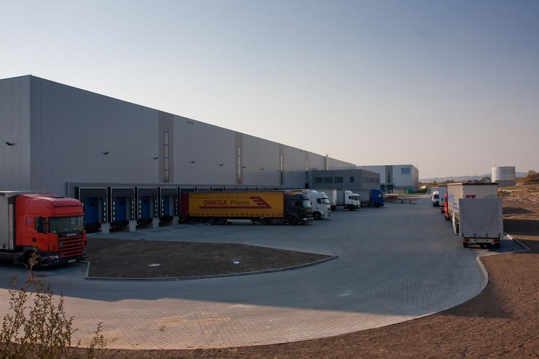 Zdjęcie ukazuje plac manewrowy Goodman Kraków Airport Logistics Centre, w tle widać załadunek samochodów ciężarkowych.