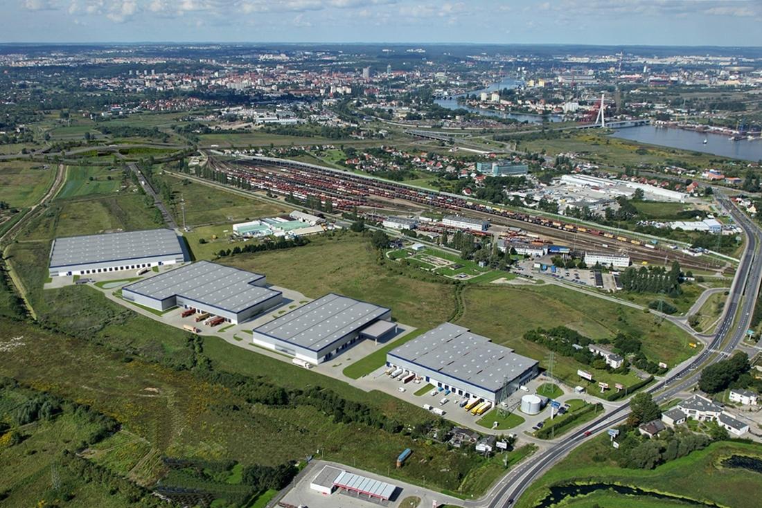 Zdjęcie przedstawia wrenderowany kompleks magazynowy Panattoni Park Gdańsk, w tle widoczna panorama miasta – Gdańsk.