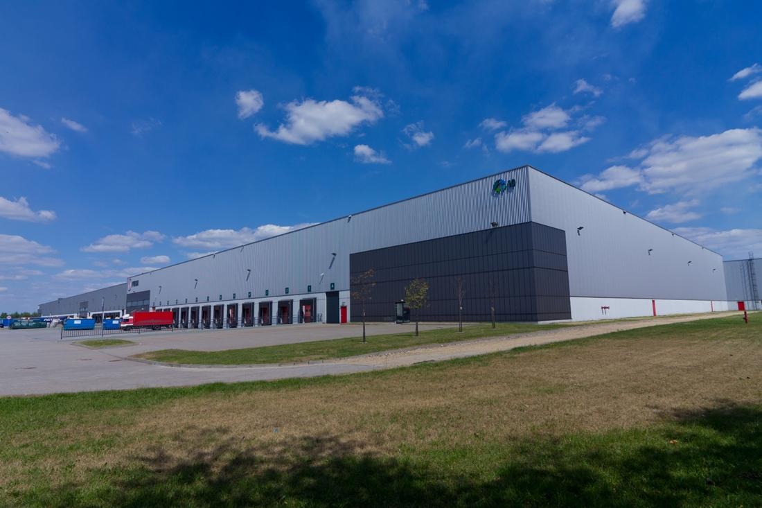 Zdjęcie ukazuje parking Prologis Park Dąbrowa, w tle obiekt magazynowy ,,nr 10’’.