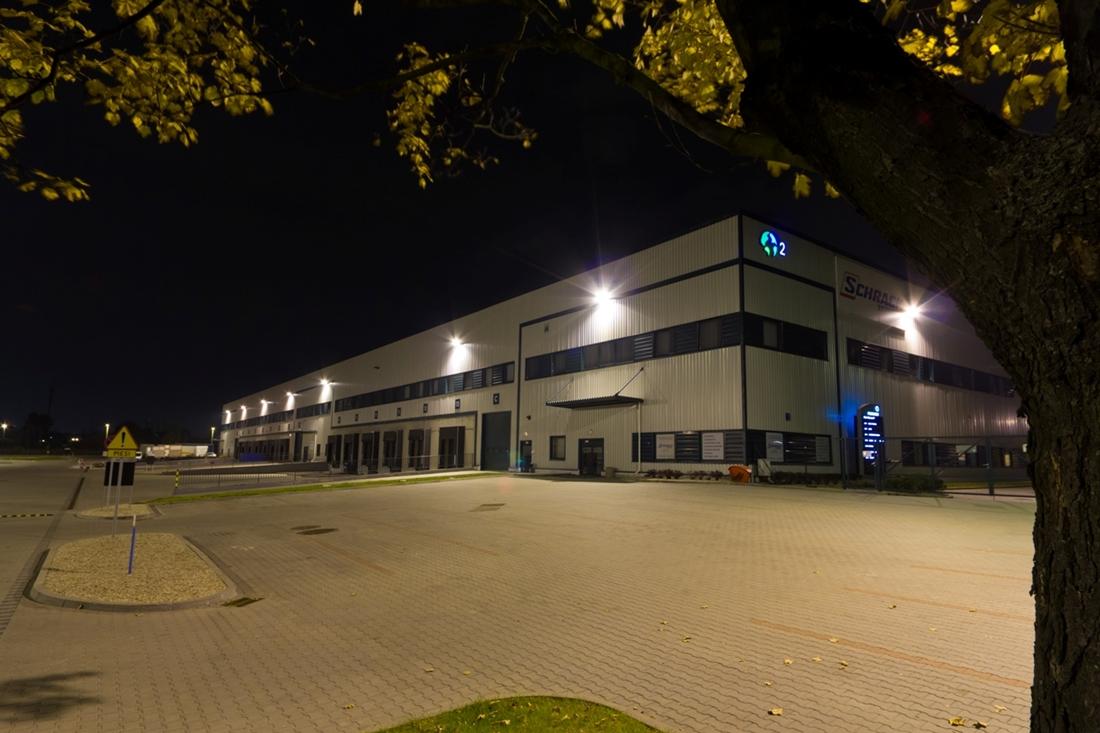 Zdjęcie prezentuje parking Prologis Park Warsaw II nocą, w tle oświetlony budynek magazynowy ''nr.2''.