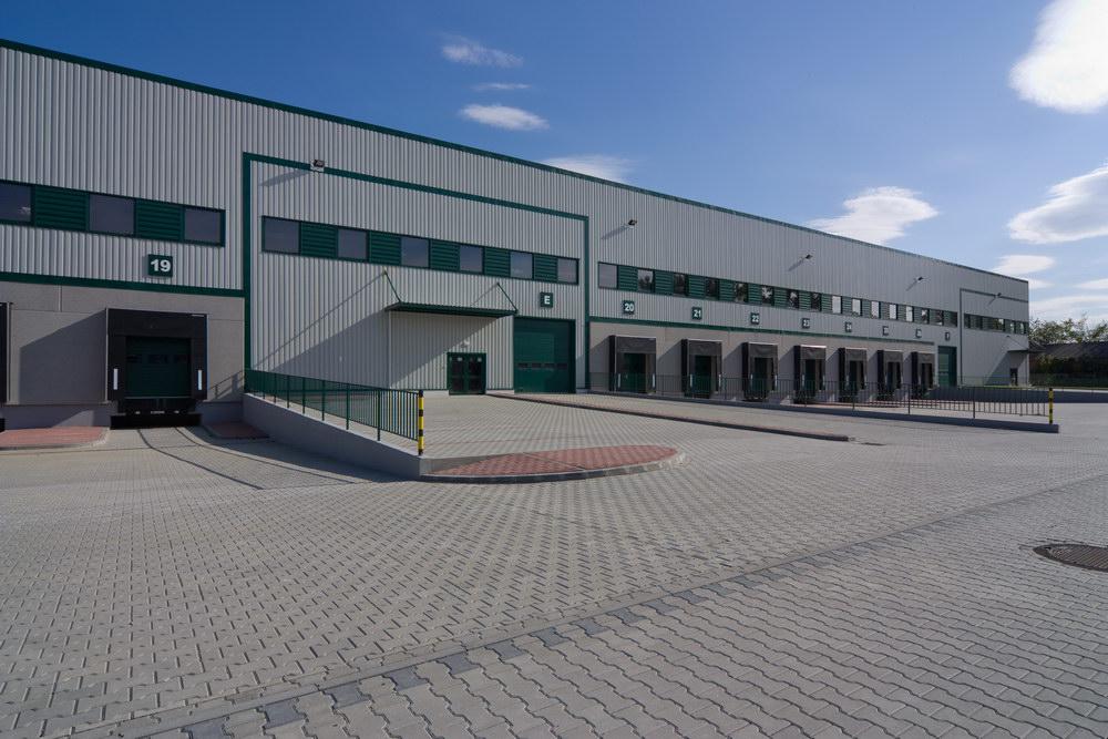 Zdjęcie przedstawia parking Prologis Park Warsaw II, w tle budynek magazynowy ''nr.1'' z nowoczesnymi dokami.