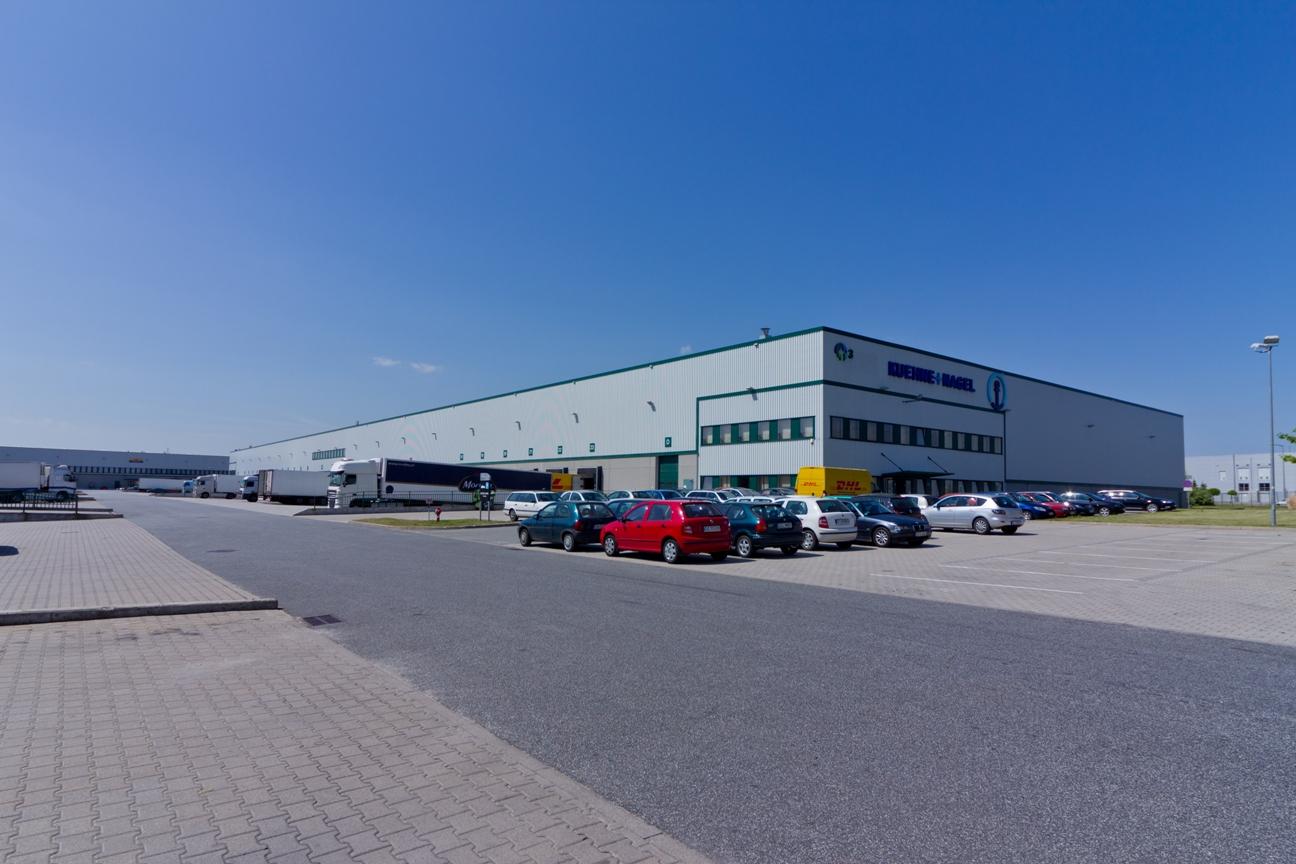 Zdjęcie przedstawia samochody na parkingu oraz plac manewrowy Prologis Park Wrocław I, w tle obiekt magazynowy ''nr. 3''.
