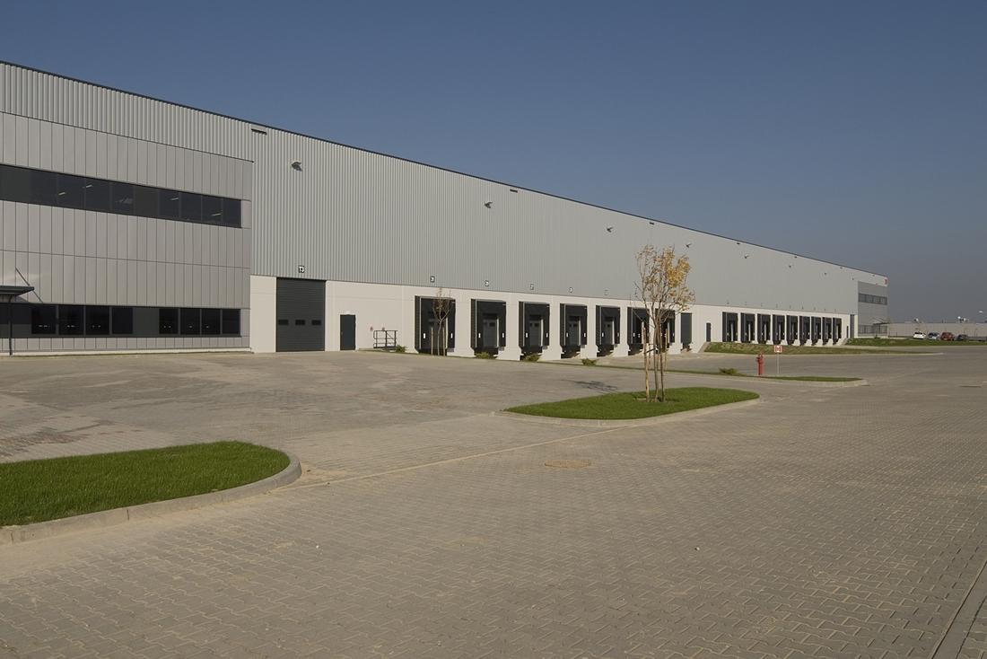 Zdjęcie ukazuje parking oraz plac manewrowy Segro Logistics Park Stryków, w tle widać budynek magazynowo-produkcyjny.