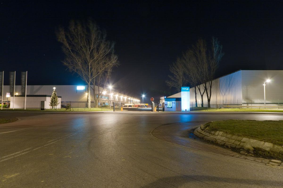 Zdjęcie ukazuje stróżówkę z bramą wjazdową Prologis Park Błonie, w tle budynek magazynowo-biurowy ''DC 1'' nocą.